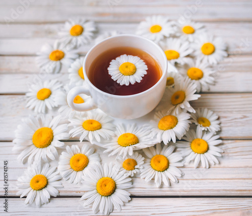 Cup of beauty chamomile tea with fresh daisies. White fresh flowers on a light gray vintage wooden background. Concept.