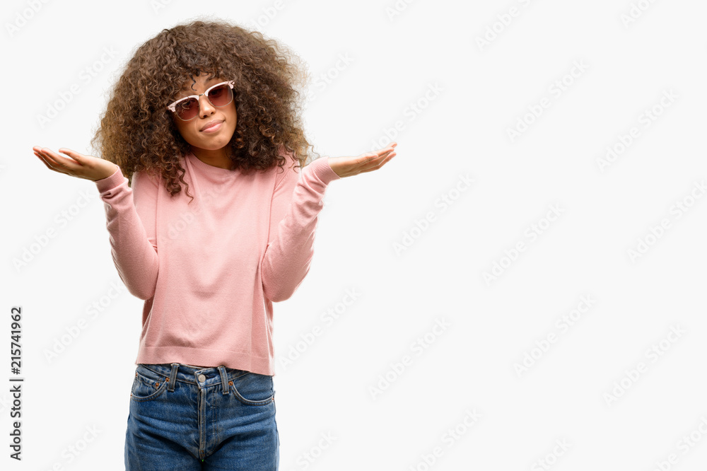 African american woman wearing pink sunglasses clueless and confused expression with arms and hands raised. Doubt concept. African american woman wearing pink sunglasses clueless and confused expression with arms and hands raised. Doubt concept.