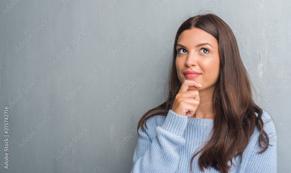 Young brunette woman over grunge grey wall serious face thinking about question, very confused idea