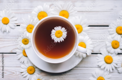Cup of chamomile tea with fresh daisies. White fresh flowers on a gray vintage wooden background. Concept, top view.