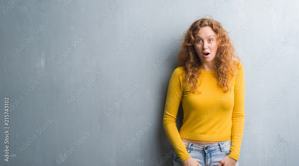 Young redhead woman over grey grunge wall afraid and shocked with surprise expression, fear and excited face.