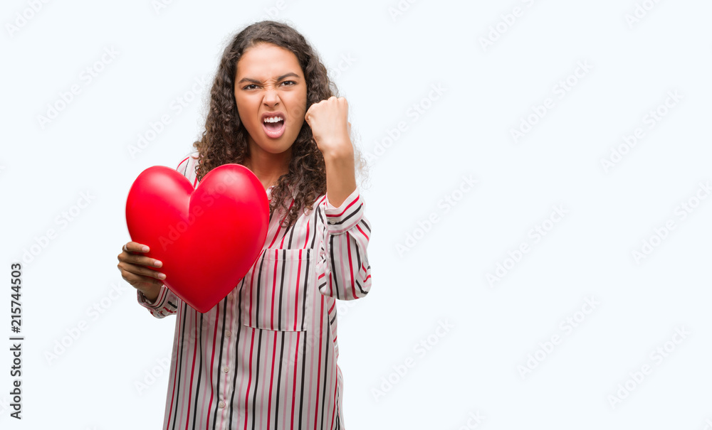 Young hispanic woman in love holding red heart annoyed and frustrated shouting with anger, crazy and yelling with raised hand, anger concept Young hispanic woman in love holding red heart annoyed and frustrated shouting with anger, crazy and yelling with raised hand, anger concept