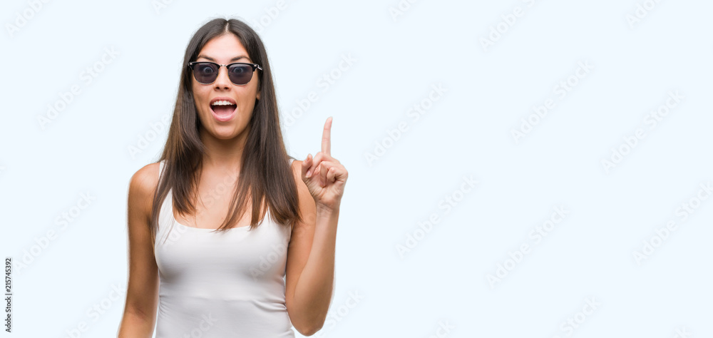 Young beautiful hispanic wearing sunglasses pointing finger up with successful idea. Exited and happy. Number one.