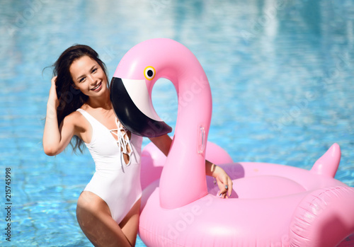 Young sexy pretty woman relaxing in a swimming pool leisure with giant inflatable giant pink flamingo float mattress in white bikini © Dmitry Lobanov