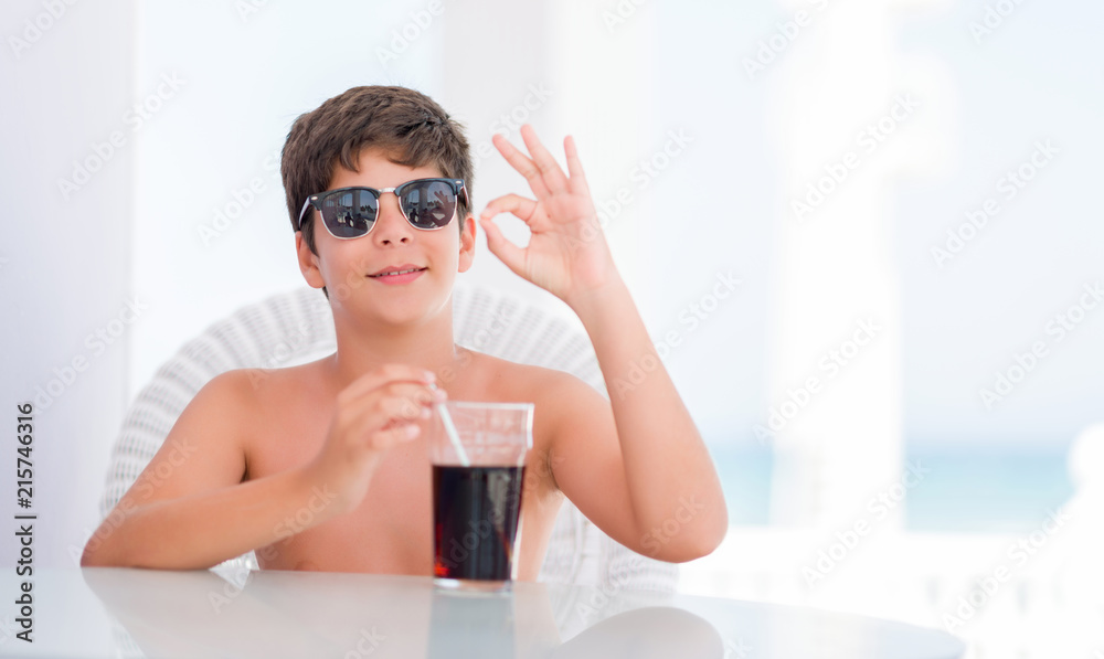 Young child on holidays drinking soda doing ok sign with fingers, excellent symbol Young child on holidays drinking soda doing ok sign with fingers, excellent symbol