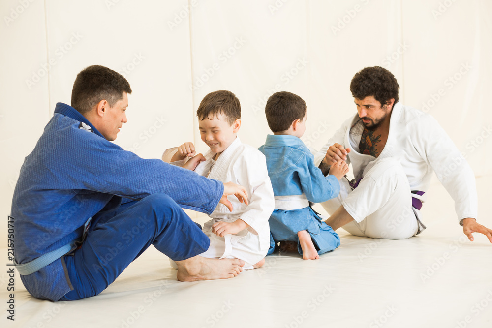 Male karate instructors training little children boys in dojo or jiu-jitsu at gym at tatami. Trainer teaches kid the basics of fighting for self-defense. Group of man and kids in sambo training Male karate instructors training little children boys in dojo or jiu-jitsu at gym at tatami. Trainer teaches kid the basics of fighting for self-defense. Group of man and kids in sambo training