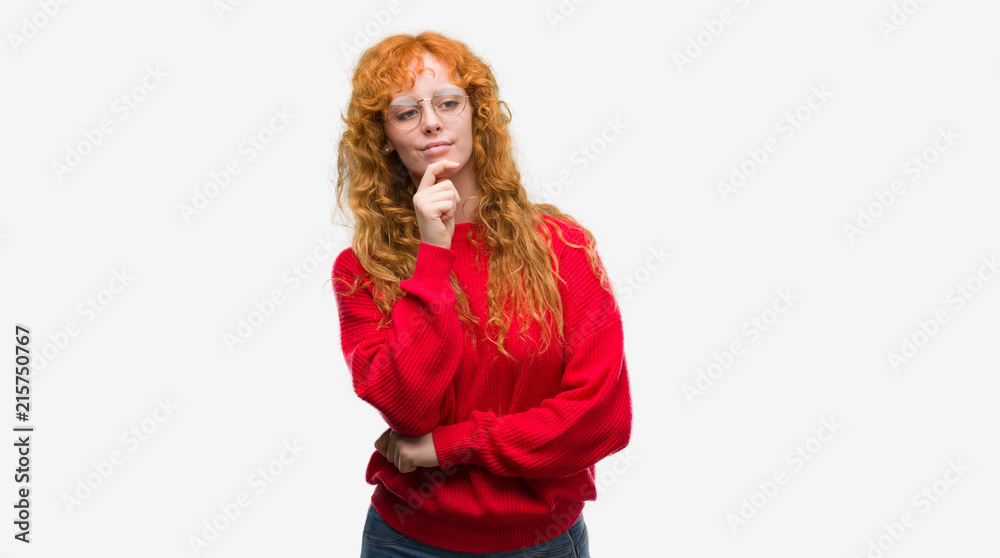 Young redhead woman wearing red sweater looking confident at the camera with smile with crossed arms and hand raised on chin. Thinking positive. Young redhead woman wearing red sweater looking confident at the camera with smile with crossed arms and hand raised on chin. Thinking positive.