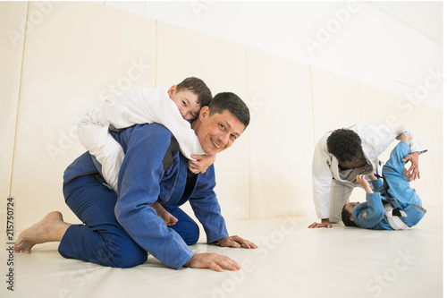 Male karate instructors training little children boys in dojo or jiu-jitsu at gym at tatami. Trainer teaches kid the basics of fighting for self-defense. Group of man and kids in sambo training