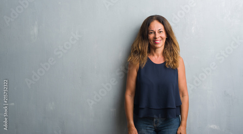 Middle age hispanic woman standing over grey grunge wall with a happy and cool smile on face. Lucky person.