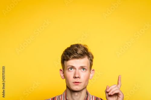look up. funny comic man pointing upward with a hand. portrait of a young guy on yellow background popping up or peeking out from the bottom. free space for advertisement.