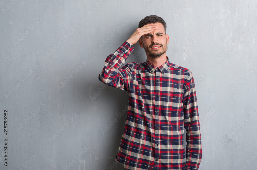 Young adult man standing over grey grunge wall stressed with hand on head, shocked with shame and surprise face, angry and frustrated. Fear and upset for mistake.