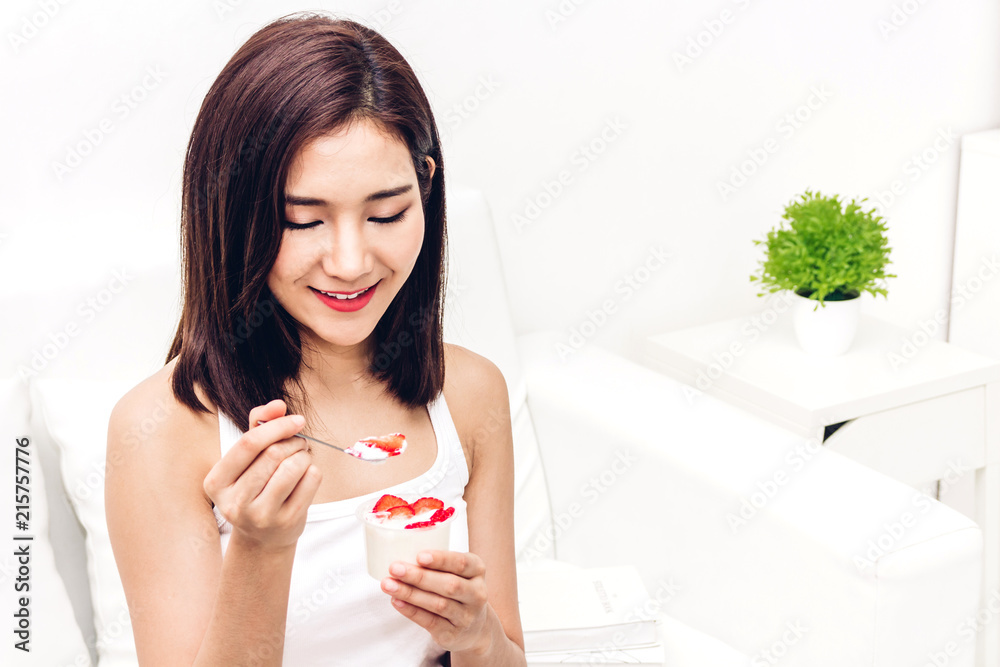 Woman eating yogurt with fresh strawberry while relaxing on sofa at home.dieting concept.healthy lifestyle Woman eating yogurt with fresh strawberry while relaxing on sofa at home.dieting concept.healthy lifestyle