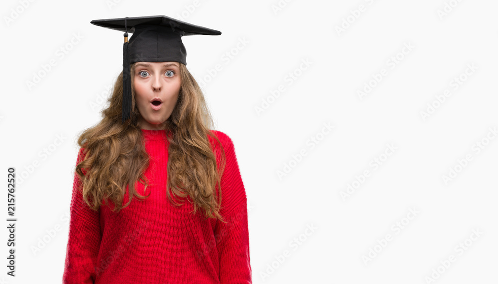 Young blonde woman wearing graduation cap scared in shock with a surprise face, afraid and excited with fear expression