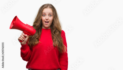 Young blonde woman holding red megaphone scared in shock with a surprise face, afraid and excited with fear expression