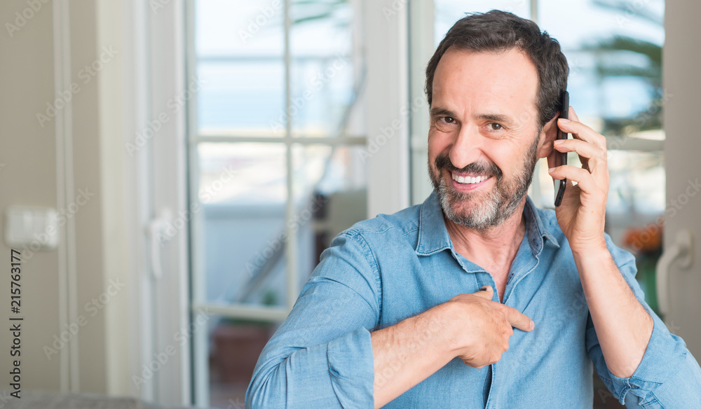Middle age man using smartphone with surprise face pointing finger to himself Middle age man using smartphone with surprise face pointing finger to himself