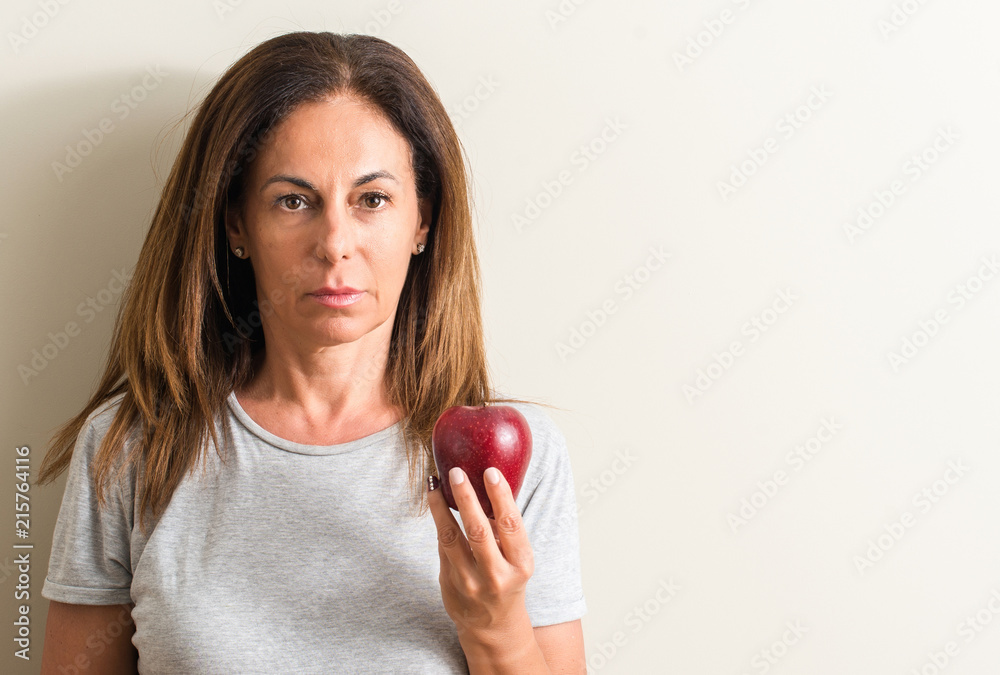Middle age woman holding a green apple with a confident expression on smart face thinking serious Middle age woman holding a green apple with a confident expression on smart face thinking serious
