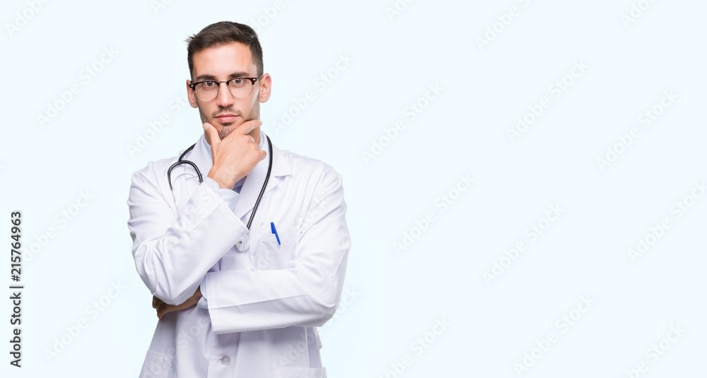 Handsome young doctor man looking confident at the camera with smile with crossed arms and hand raised on chin. Thinking positive. Handsome young doctor man looking confident at the camera with smile with crossed arms and hand raised on chin. Thinking positive.