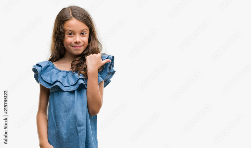 Brunette hispanic girl wearing denim dress pointing and showing with thumb up to the side with happy face smiling Brunette hispanic girl wearing denim dress pointing and showing with thumb up to the side with happy face smiling