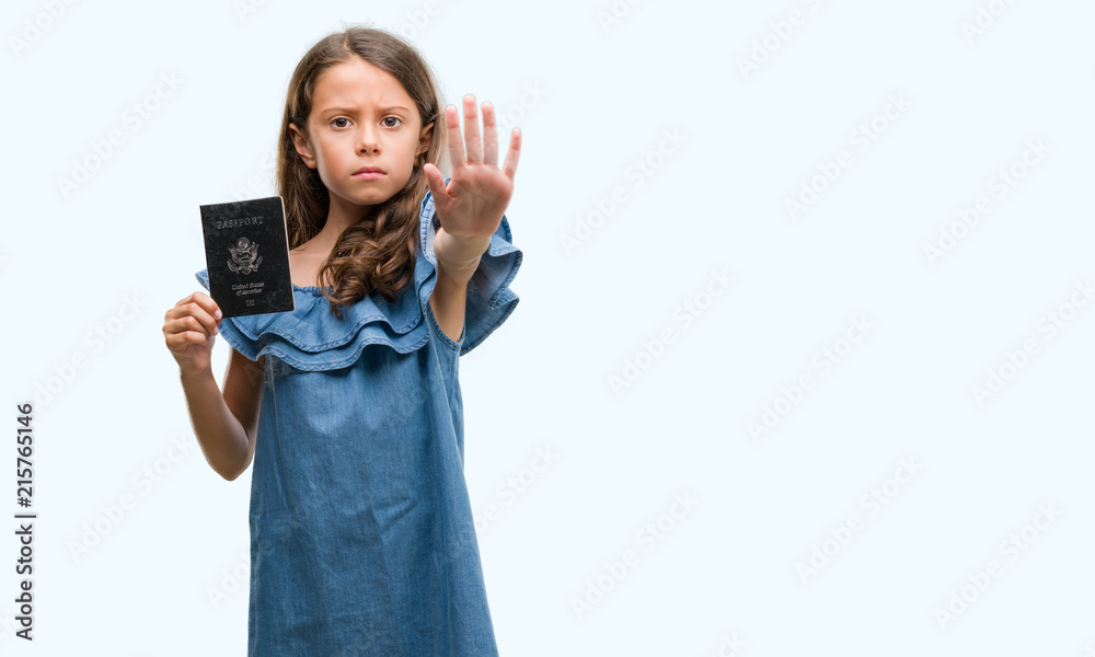 Brunette hispanic girl holding passport of United States of America with open hand doing stop sign with serious and confident expression, defense gesture