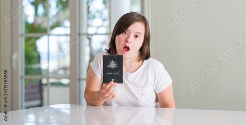Down syndrome woman at home holding australian passport scared in shock with a surprise face, afraid and excited with fear expression
