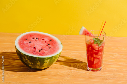 close up view of fresh watermelon and watermelon drink in glass on wooden surface on yellow background