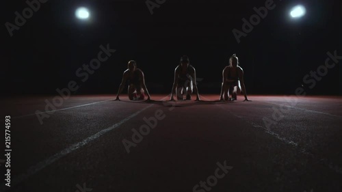 Three girls in black clothes are in the starting pads to start the race in the competition in the light of the lights and run towards the finish photo