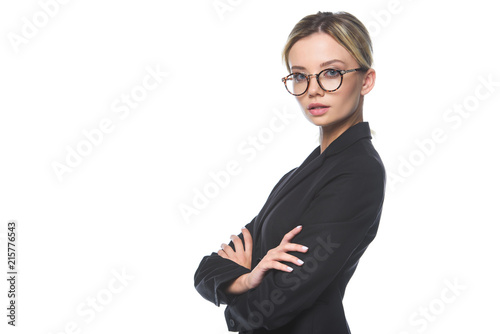 confident young businesswoman in suit and eyeglasses looking at camera with crossed arms isolated on white