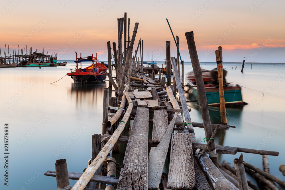 Old wood bridge for small fishing boat in the sea with sunset
