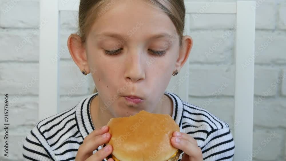 Child Eating Hamburger in Restaurant, Kid Eats Junk Fast Food Hungry Little Girl Child Eating Hamburger in Restaurant, Kid Eats Junk Fast Food Hungry Little Girl