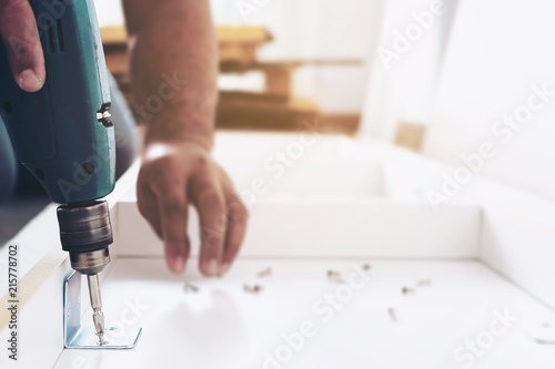 Man is working with furniture assembly using electric screwdriver in new house installation - technician onsite work using hand tools concept