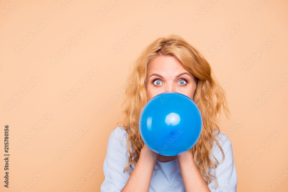 Attractive beautiful cute nice curly-haired cheerful blonde caucasian young girl blowing blue air ball. Copy space. Isolated over grey background Attractive beautiful cute nice curly-haired cheerful blonde caucasian young girl blowing blue air ball. Copy space. Isolated over grey background