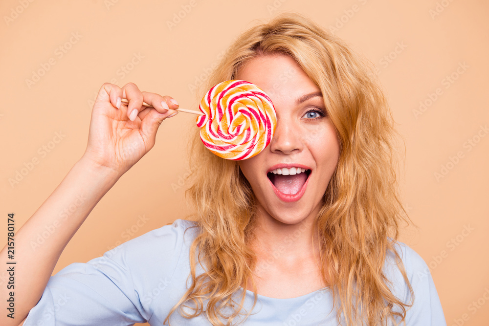 Portrait of attractive beautiful cute nice curly-haired cheerful blonde caucasian young girl with round lollypop. Isolated over grey background