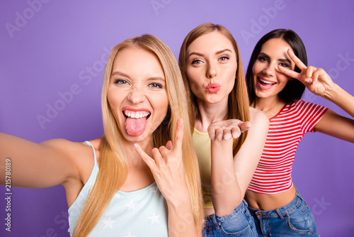 Self portrait of funky cool girls gesturing tongue out rock and roll symbol v-sign sending air kiss with pout lips palm isolated on bright violet background. Rest relax leisure concept