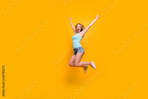 Full-legh portrait of cute blondy girl happily jump and rejoices of victory rise up fists isolated on bright yellow background with copy space for text © deagreez