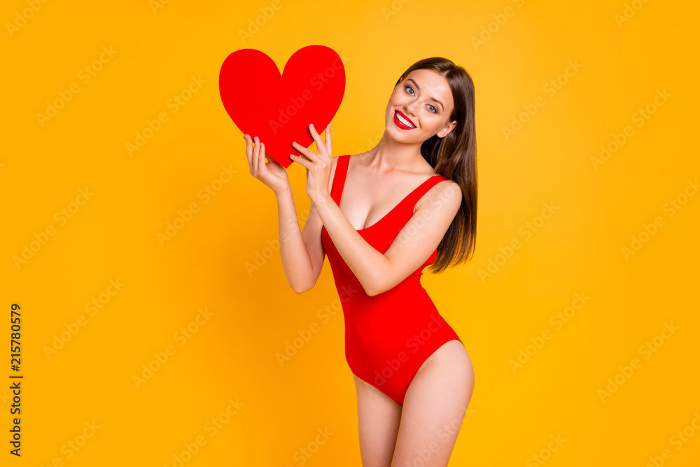Portrait of lovely woman with big paper carton red heart in hand looking at camera isolated on yellow vivid background Portrait of lovely woman with big paper carton red heart in hand looking at camera isolated on yellow vivid background