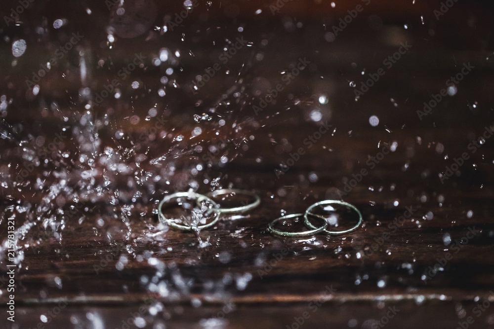 Double white gold wedding rings under water drops splash close up. Studio macro shot on wooden texture Double white gold wedding rings under water drops splash close up. Studio macro shot on wooden texture