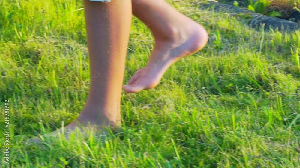 bare feet of the boy are walking along a green lawn in a summer sunny day bare feet of the boy are walking along a green lawn in a summer sunny day