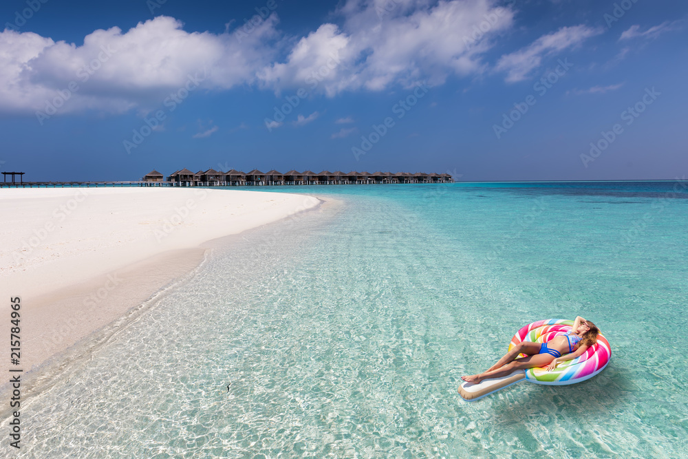 Junge Frau im Bikini genießt ihren Urlaub auf den Malediven auf einem schwimmenden Lolli über türkisem Ozean