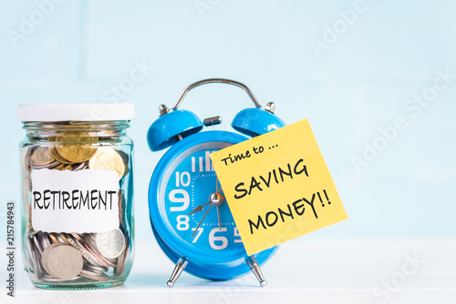 Glass jar coins and alarm clock with time to saving money text for retirement concept.