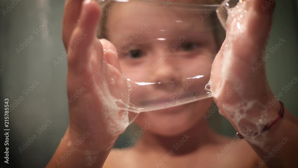Child girl play make blow big soap bubbles with her hands in bathroom, stretch, collide and burst them Child girl play make blow big soap bubbles with her hands in bathroom, stretch, collide and burst them