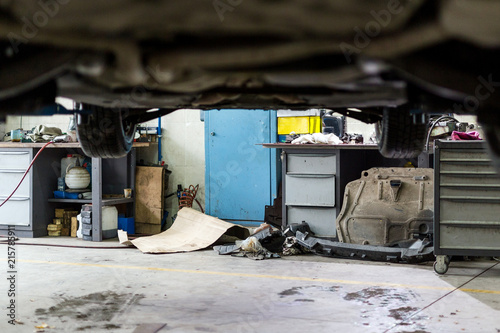 Car hanged on lift at service station. Dirty vehicle  maintenance center. Disorder, mud, stains and chaos. Unprofessional clumsy automobile workshop