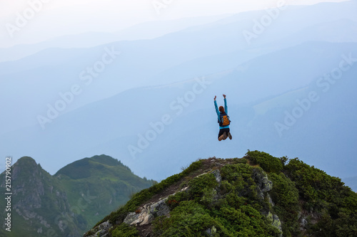 Funny frozen poses while jumping. The girl in tennis shoes. The lawn at the edge of the cliff with rocks. Vastness with mountains. Fantastic summer scenery.