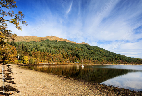 Early morning light on the autumn colours of Ardgartan woods reflected in the calm waters of Loch Long 