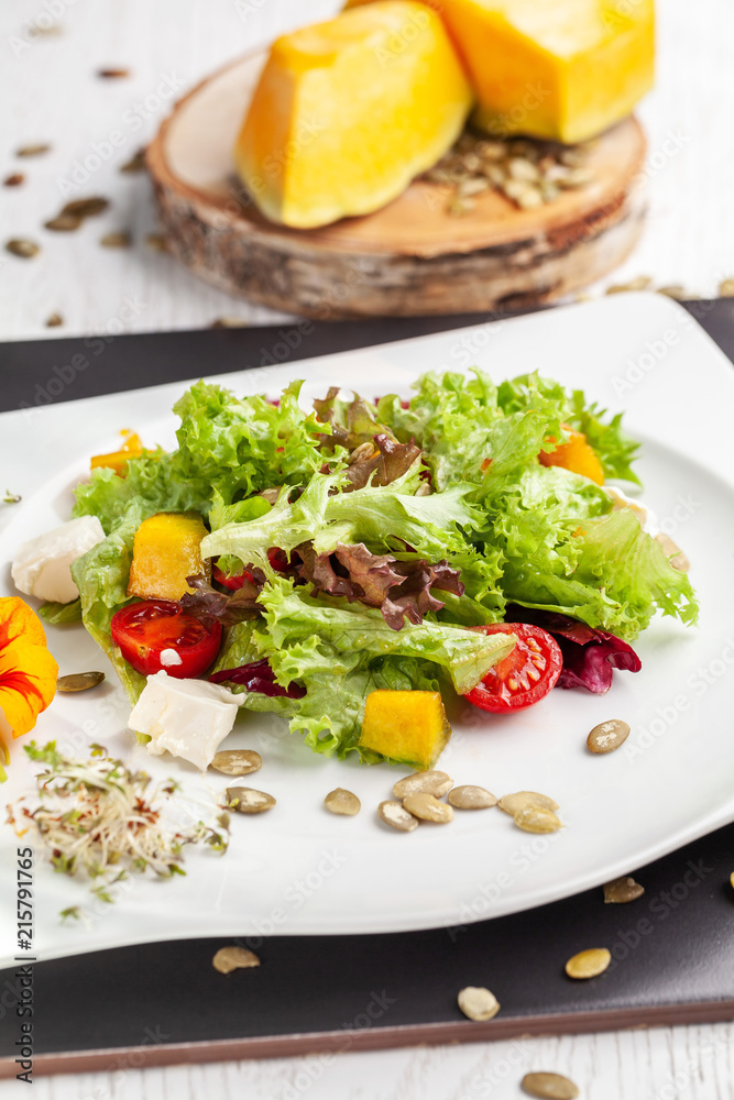 European Italian salad of lettuce, cherry tomatoes, pumpkin, edible pumpkin flowers, and pumpkin seeds, in a white plate. Copy space, selective focus European Italian salad of lettuce, cherry tomatoes, pumpkin, edible pumpkin flowers, and pumpkin seeds, in a white plate. Copy space, selective focus