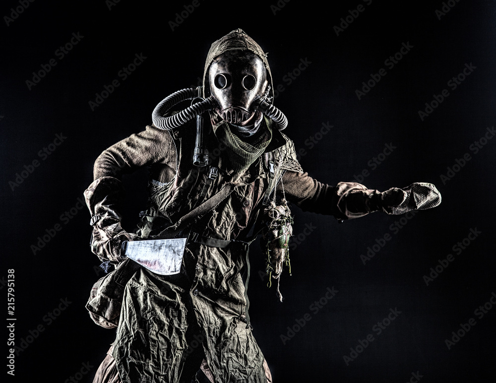 Low key portrait of post apocalyptic creature, living in catacombs mutant, survived in nuclear disaster human in ragged cloth and gas mask, armed with handmade cold weapon isolated on black background Low key portrait of post apocalyptic creature, living in catacombs mutant, survived in nuclear disaster human in ragged cloth and gas mask, armed with handmade cold weapon isolated on black background
