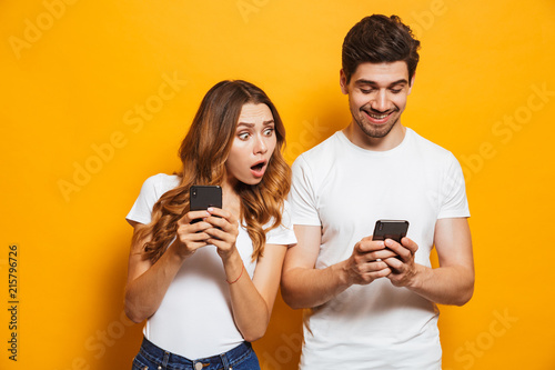 Obraz na plátně Image of young woman spying and peeking at smartphone of her boyfriend, isolated