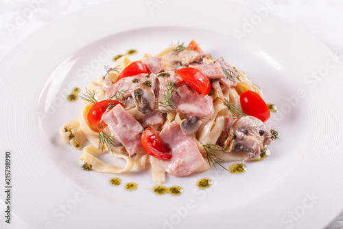 tagliatelle with mushrooms . Italian Pasta on white plate with champignons, ham and tomato