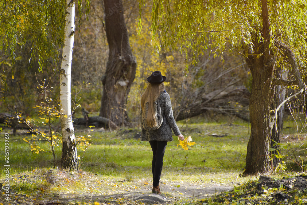 Girl in a hat with a backpack standing in the autumn forest. Back view Girl in a hat with a backpack standing in the autumn forest. Back view