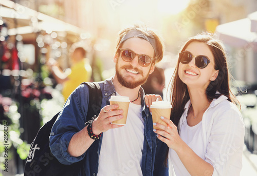 Two attractive best friends in sunglasses walking outdoors at the sunny summer street and drinking cofee