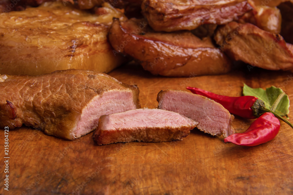 Sliced smoked meat and lard with meat veins on a wooden background with red pepper
